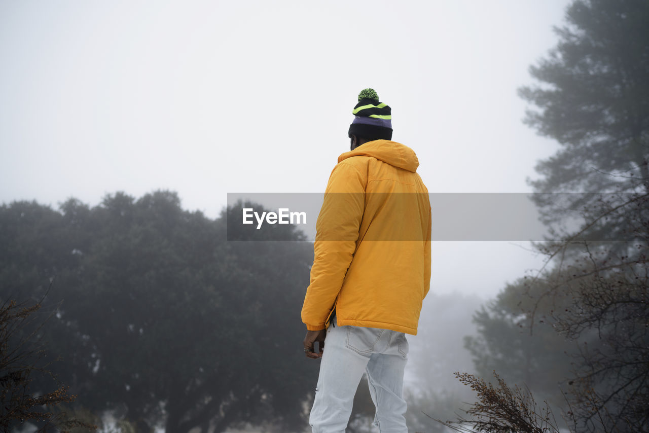 Back view of unrecognizable african american man with hands and pockets wearing outerwear standing in snowy park