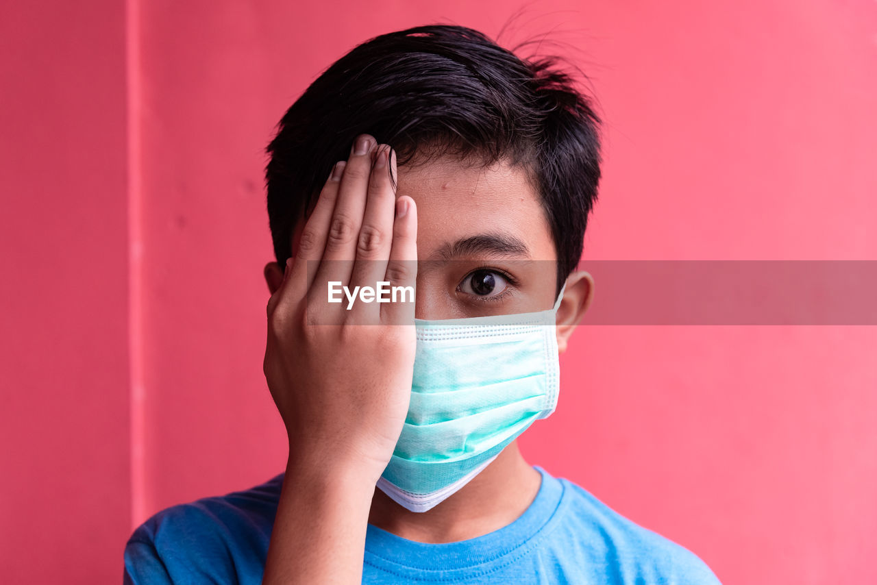 Portrait of boy covering face against red background