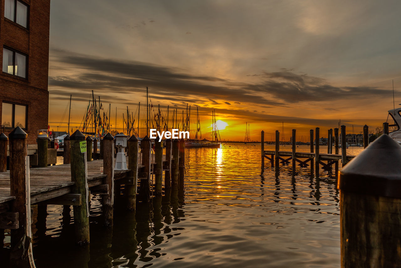 WOODEN POSTS IN SEA AGAINST SKY AT SUNSET