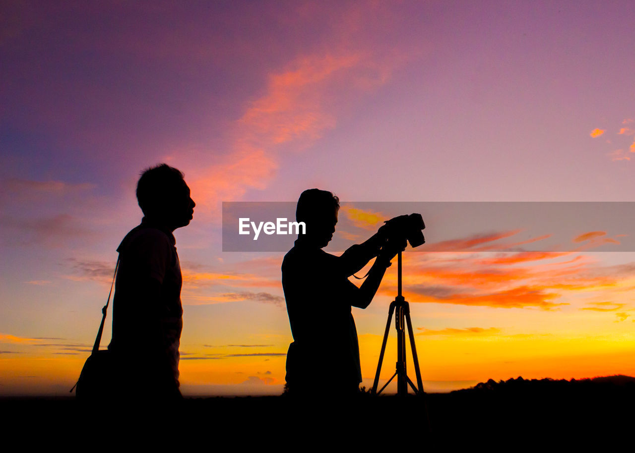 Silhouette men photographing against sky during sunset