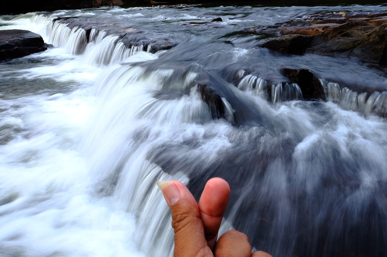 Cropped image of hand against 
waterfall