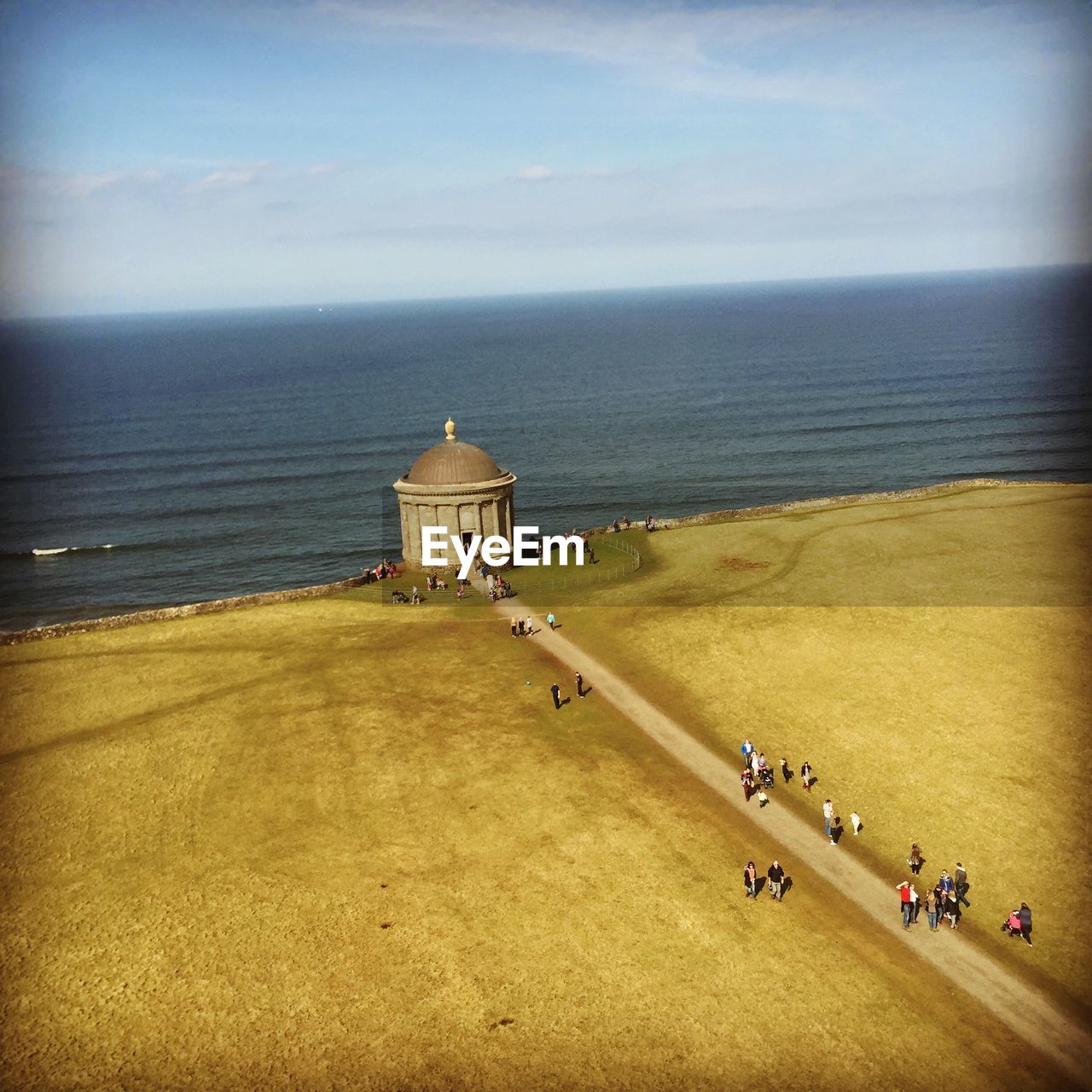 People walking on road against calm sea