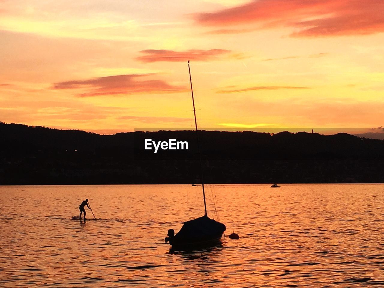 Silhouette man paddleboarding on lake zurich during sunset