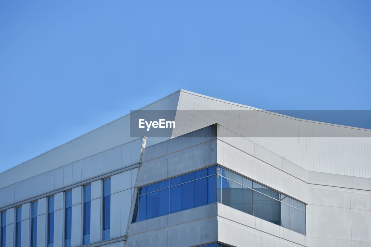 LOW ANGLE VIEW OF GLASS BUILDING AGAINST CLEAR BLUE SKY