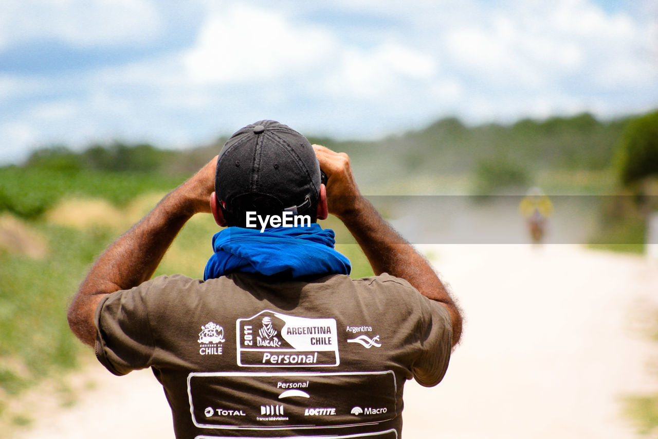 REAR VIEW OF MAN PHOTOGRAPHING AGAINST CLOUDY SKY