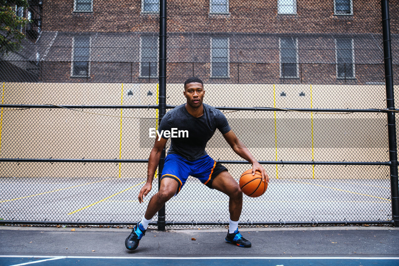 Young man playing basketball against chainlink fence