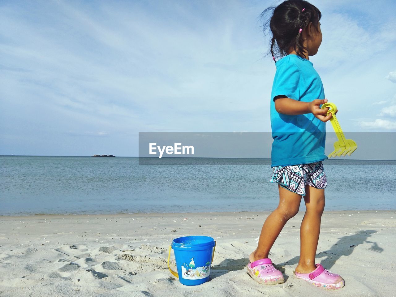 Full length of girl holding toy while standing at beach against sky