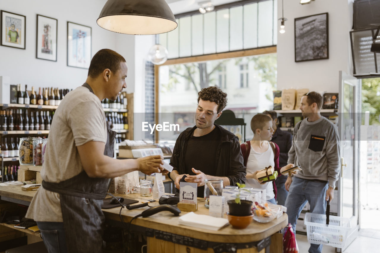 Side view of male owner explaining product to customer at checkout counter in store