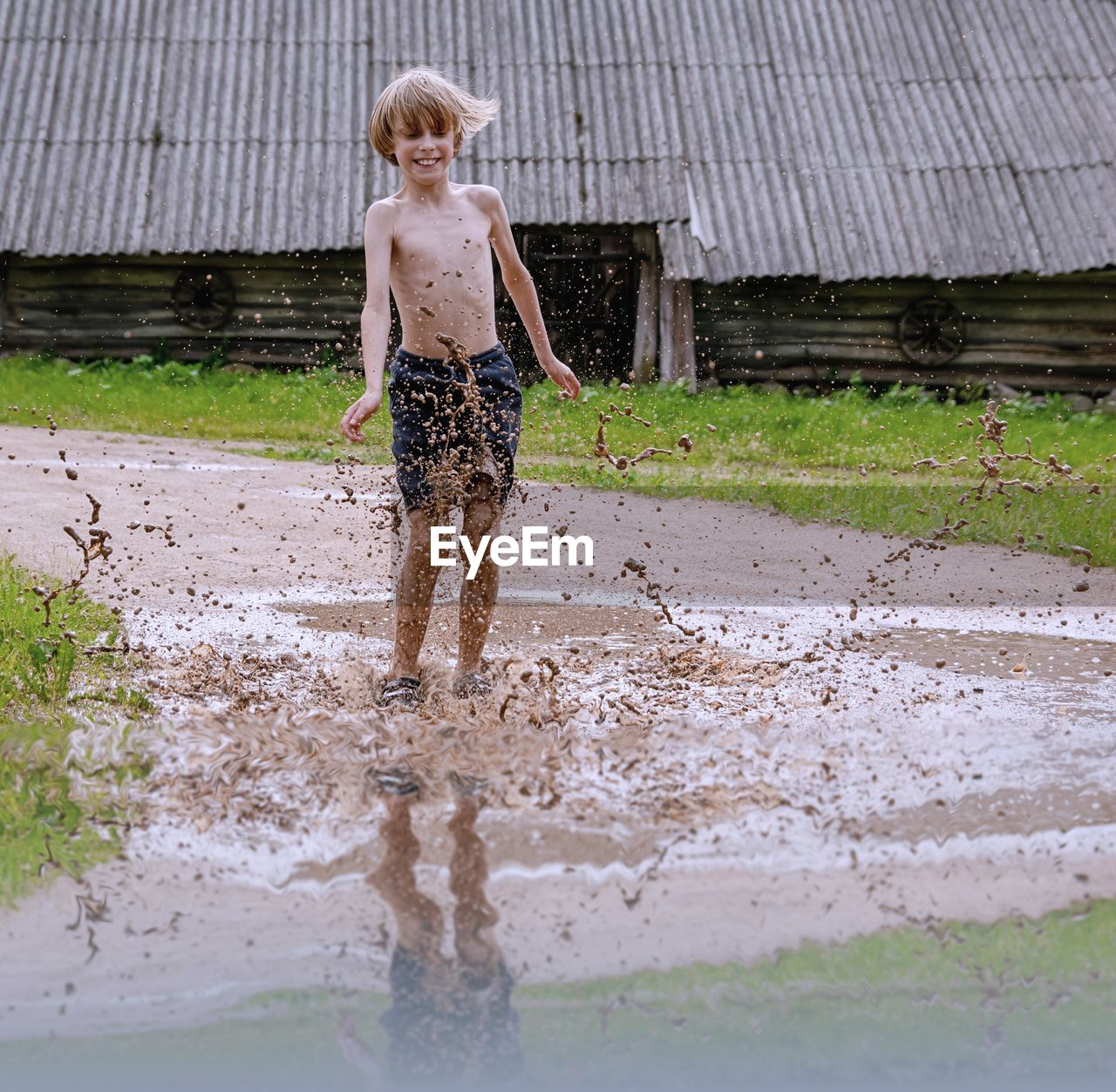 Shirtless boy splashing water while standing in puddle