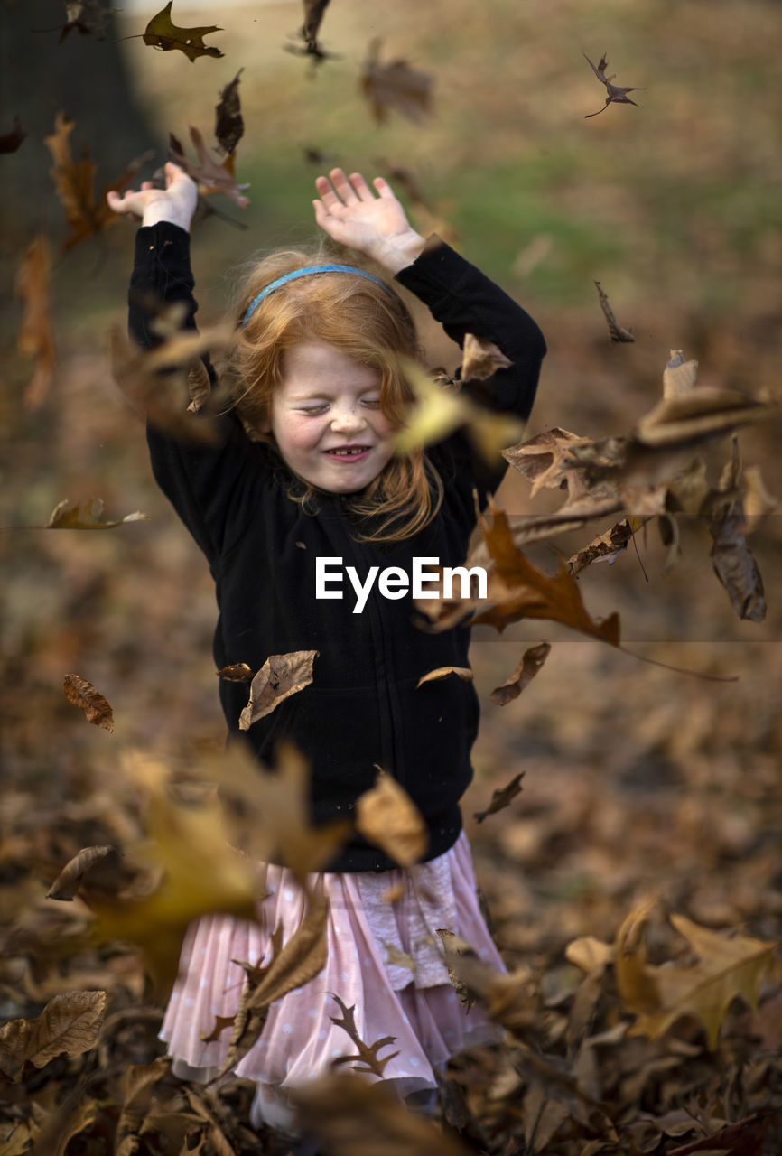 Autumn leaves falling on girl with arms raised standing at park