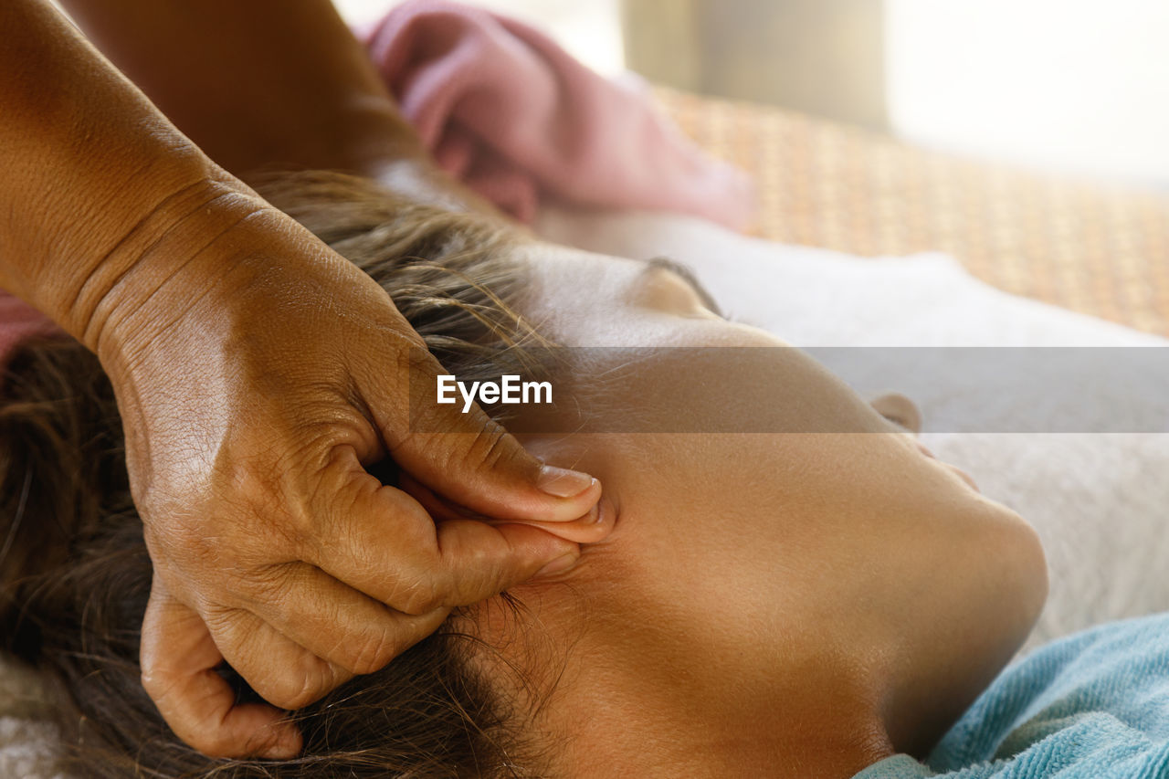 Cropped hand of massage therapist massaging woman ears at spa