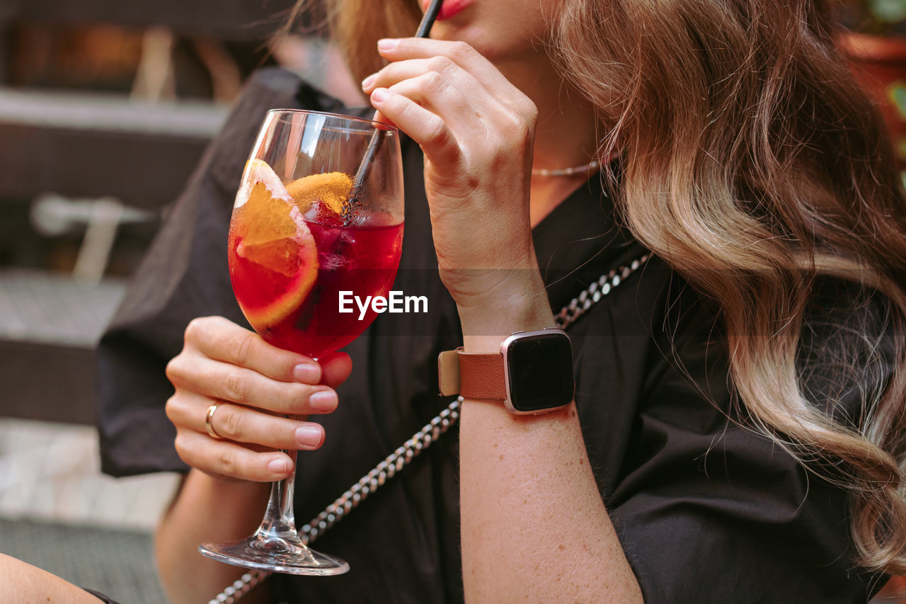 Crop female sipping fresh beverage through straw while resting on summer party.