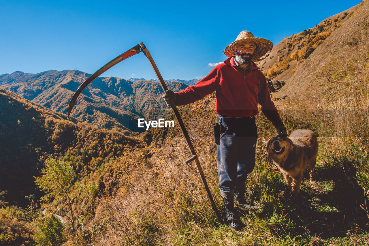 Shepherd with dog standing on landscape against clear sky