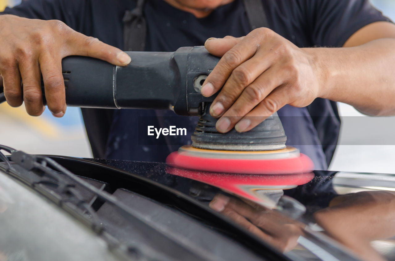 Cropped hands of mechanic polishing car in garage