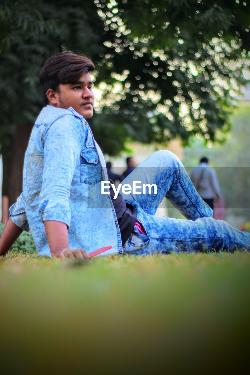 Side view of thoughtful young man looking away while sitting in park