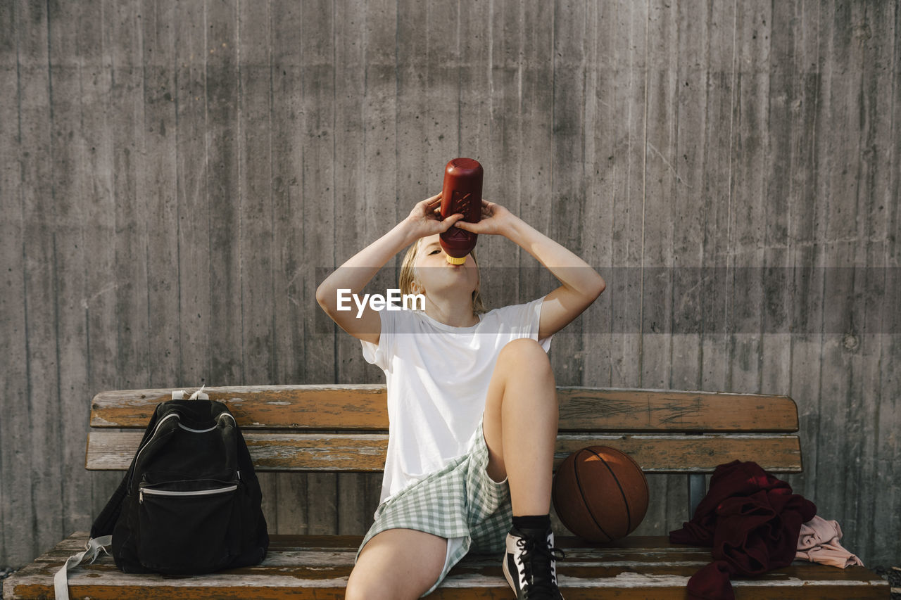 Exhausted girl drinking water while sitting on bench