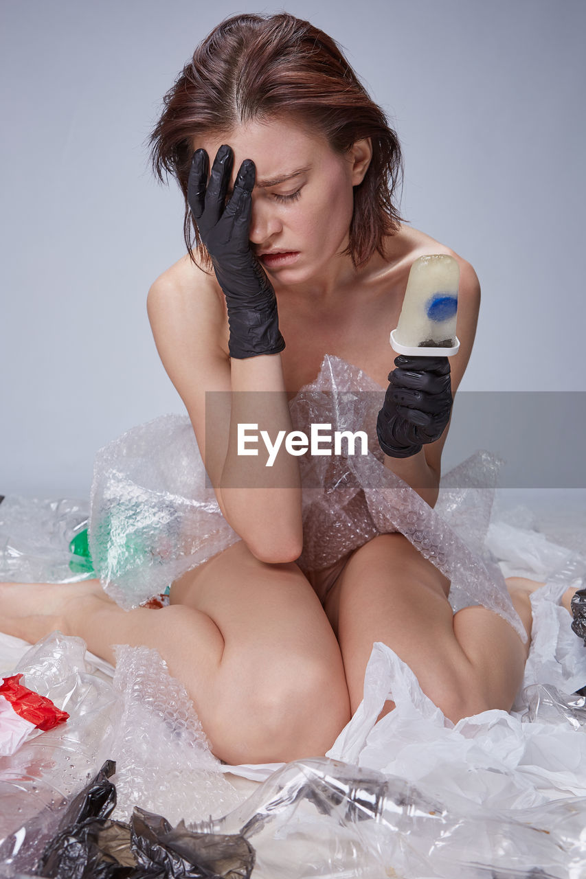 Naked young woman holding popsicle while sitting on plastics