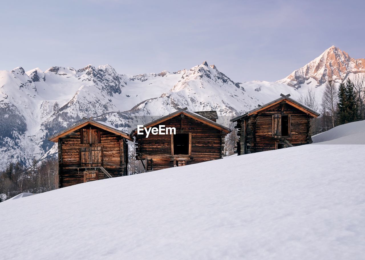 Wooden houses on snowcapped mountain against clear sky