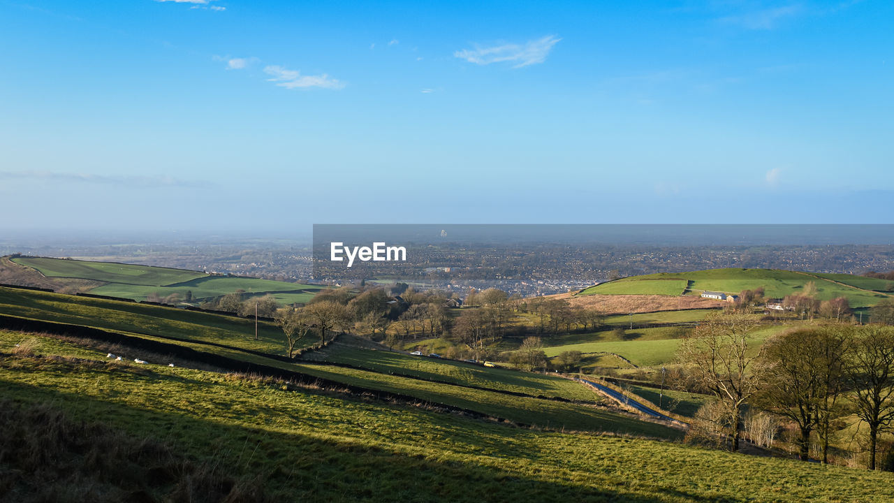 landscape, hill, environment, sky, horizon, scenics - nature, rural area, plant, land, nature, field, aerial photography, beauty in nature, plain, agriculture, rural scene, architecture, tranquility, growth, tranquil scene, green, cloud, building, no people, building exterior, morning, built structure, high angle view, day, grass, city, outdoors, farm, tree, blue, crop, idyllic, residential district, travel, sunlight, water, house, aerial view, meadow