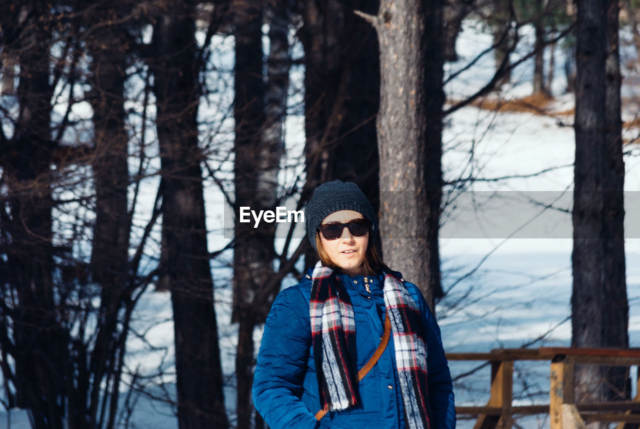 Portrait of woman standing against bare trees during winter