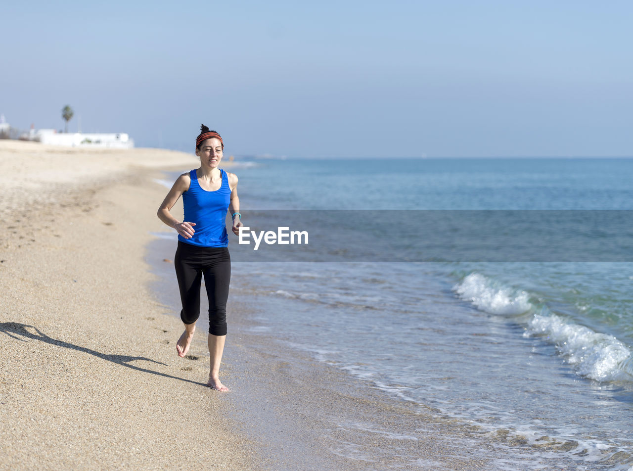 Full length of young woman jogging at beach against sky