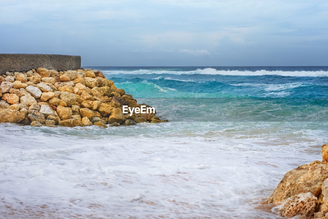 Scenic view of rocks in sea waves against sky