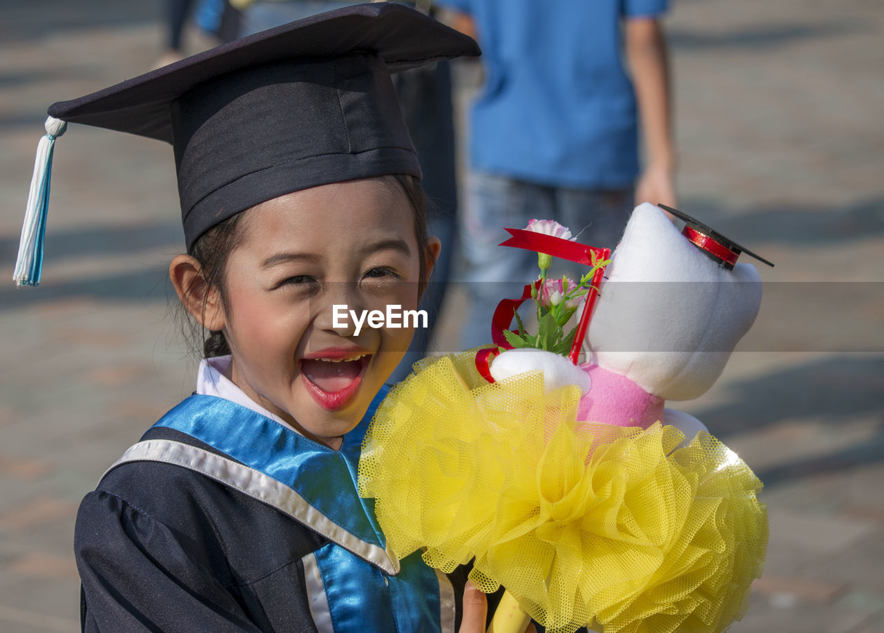 Portrait of cheerful girl wearing graduation gown holding stuffed toy