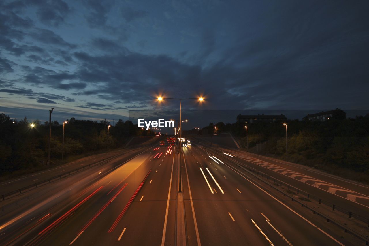 Light trails on highway against sky at dusk