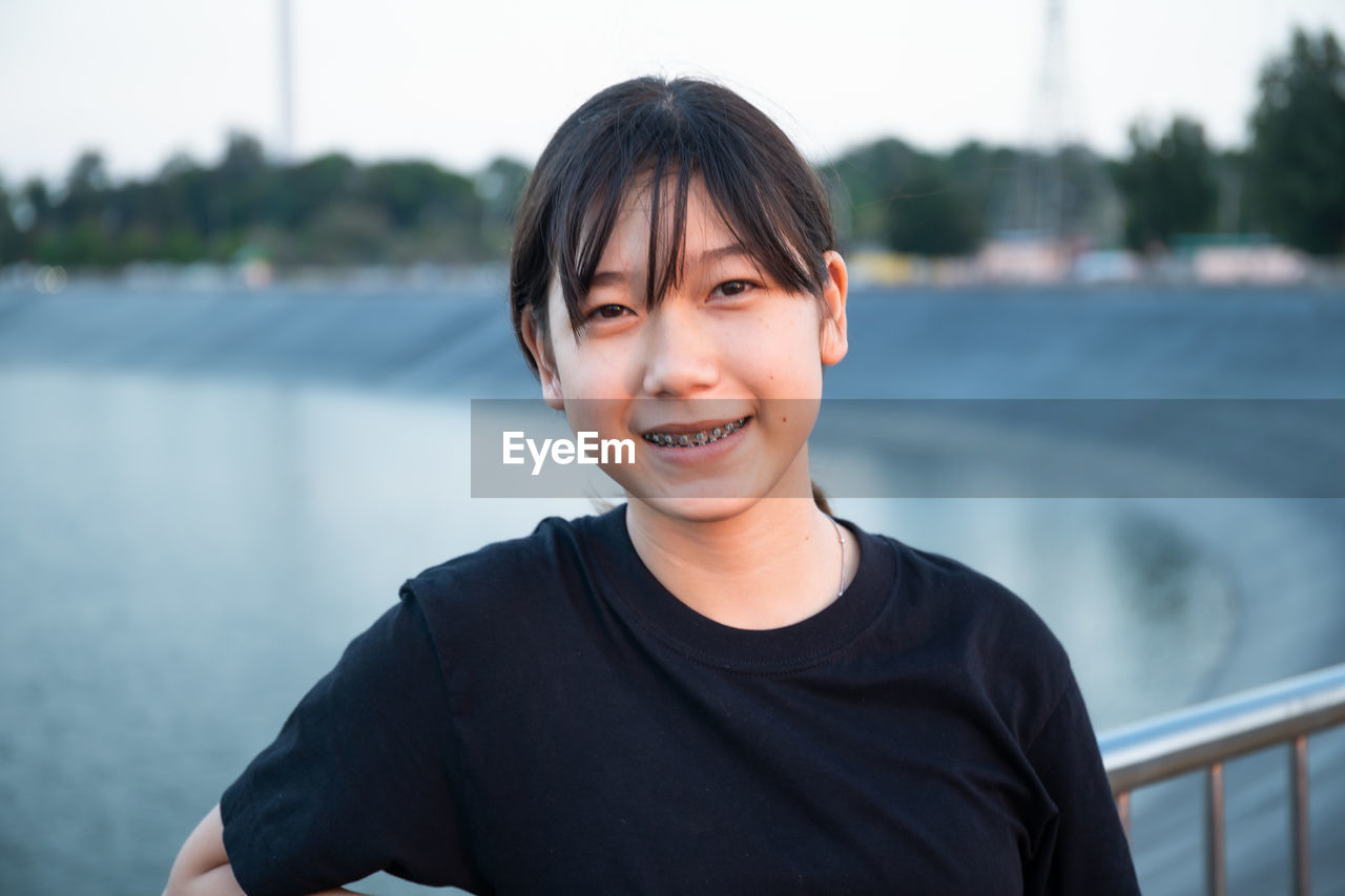 Portrait of smiling teenage girl standing by railing