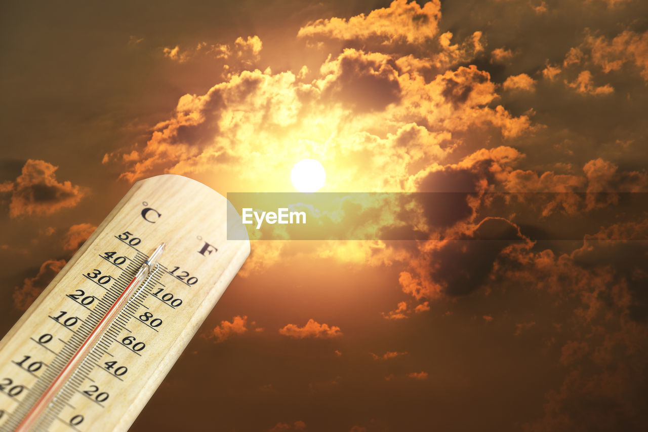 Close-up of thermometer against orange sky at sunset