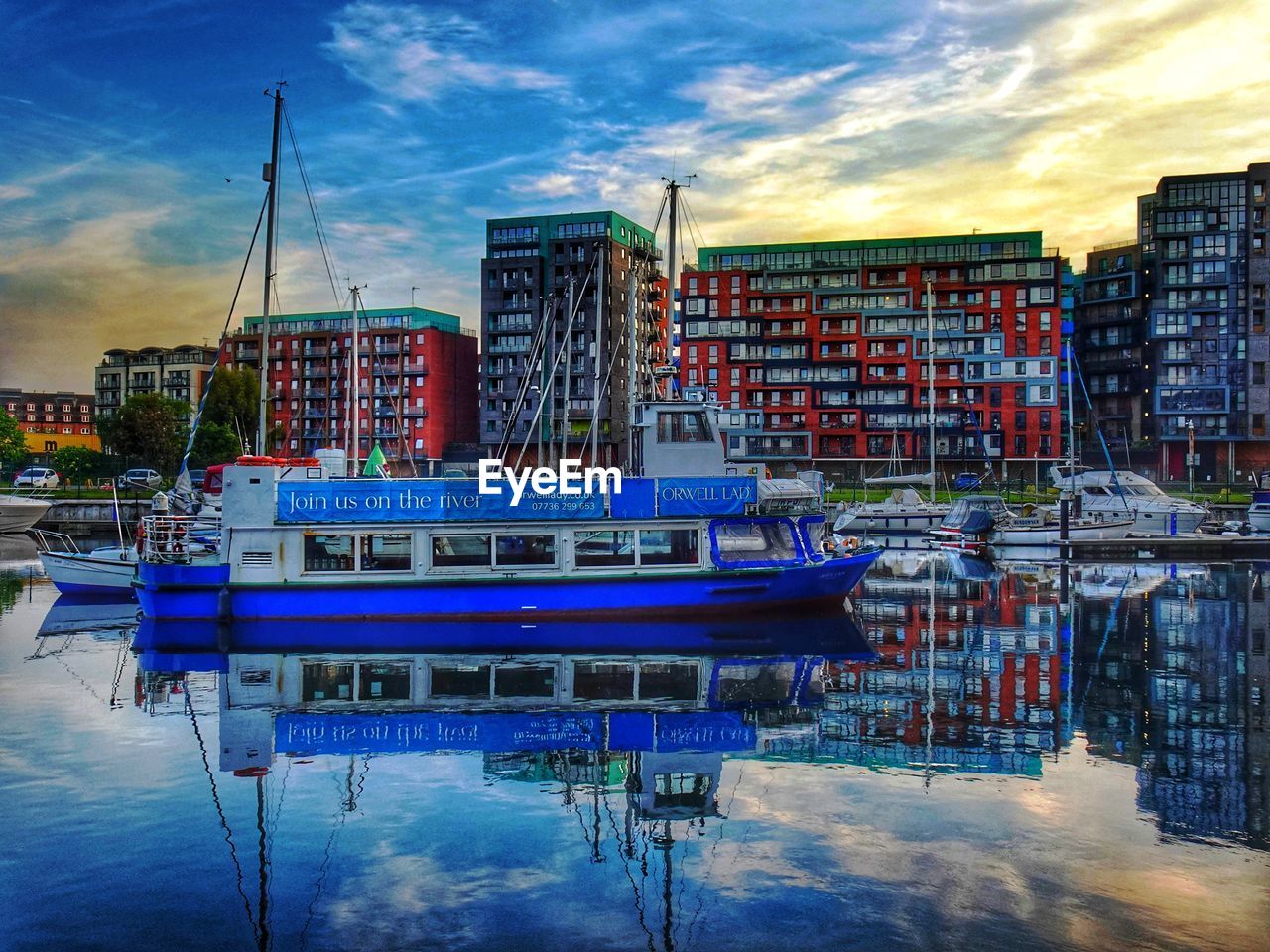 water, reflection, sky, cityscape, architecture, dock, nautical vessel, transportation, marina, harbor, cloud, building exterior, city, built structure, nature, mode of transportation, vehicle, moored, evening, building, travel destinations, waterfront, no people, ship, sunset, sea, dusk, boat, travel, outdoors, port, waterway, multi colored, blue, pier, landscape, residential district