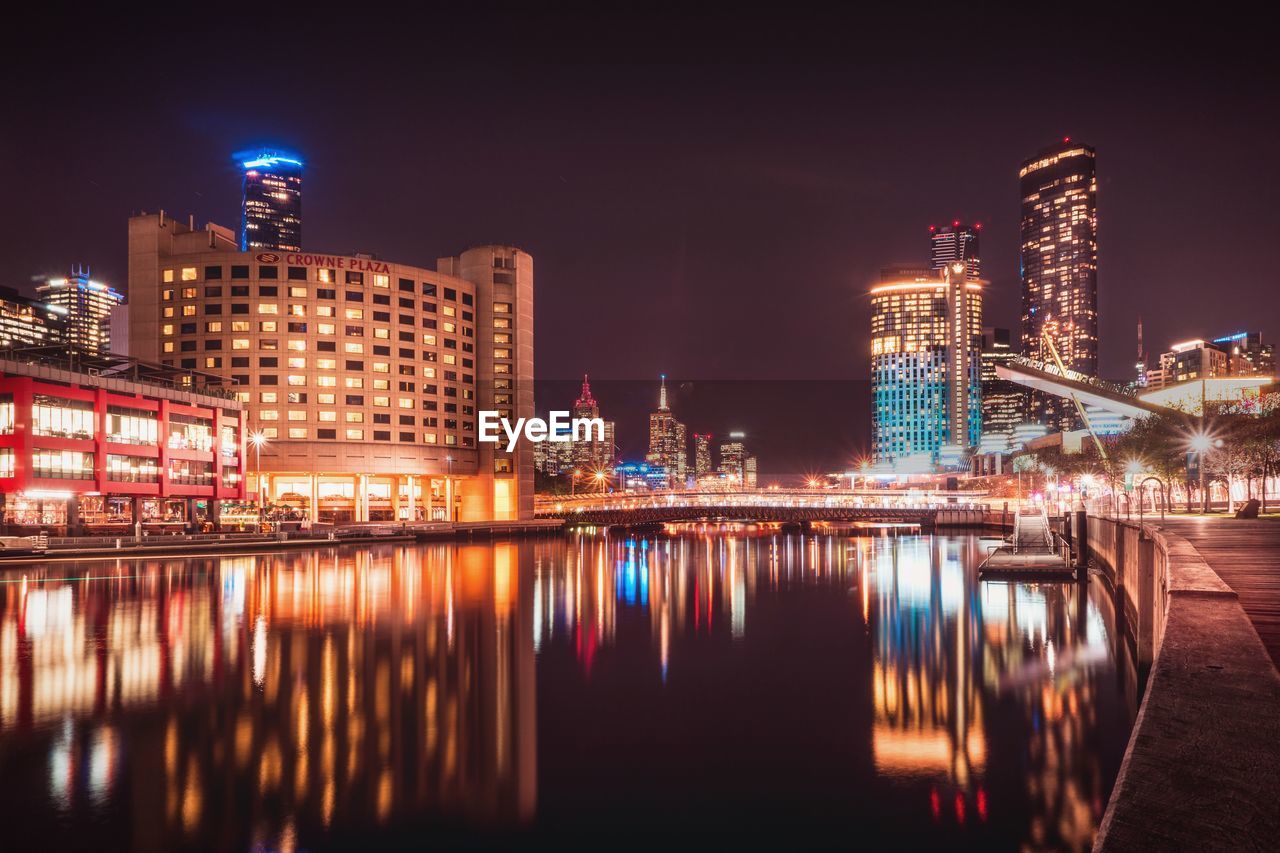 ILLUMINATED BUILDINGS BY RIVER AT NIGHT