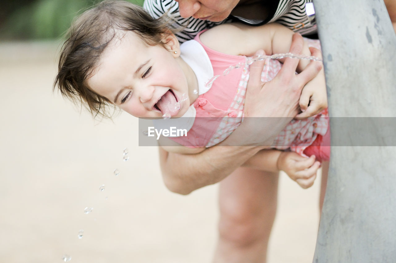 Woman holding daughter drinking water from fountain