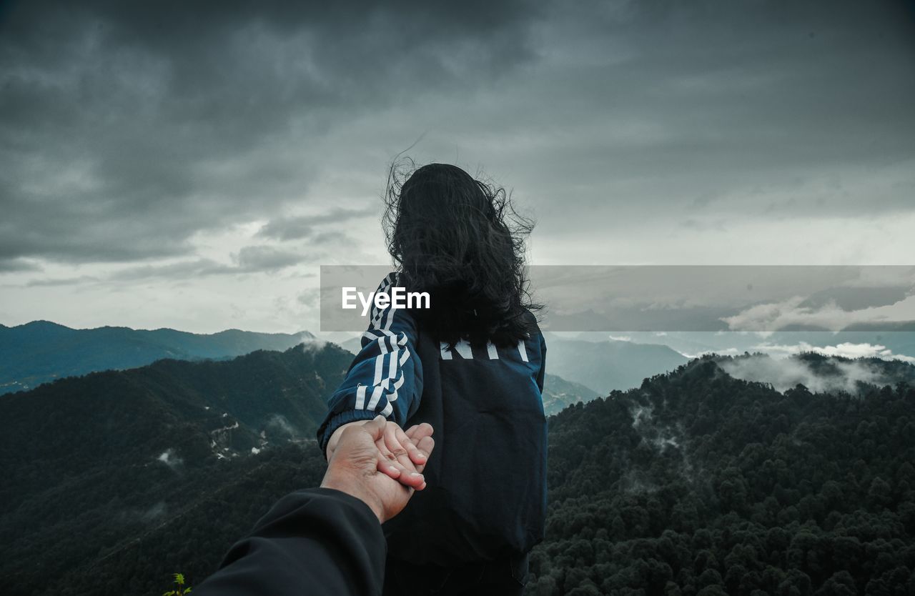 Cropped image of boyfriend holding girlfriend hand on mountain against sky