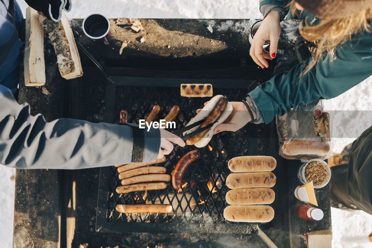 Directly above shot of man serving sausage to female friend while cooking on barbecue grill