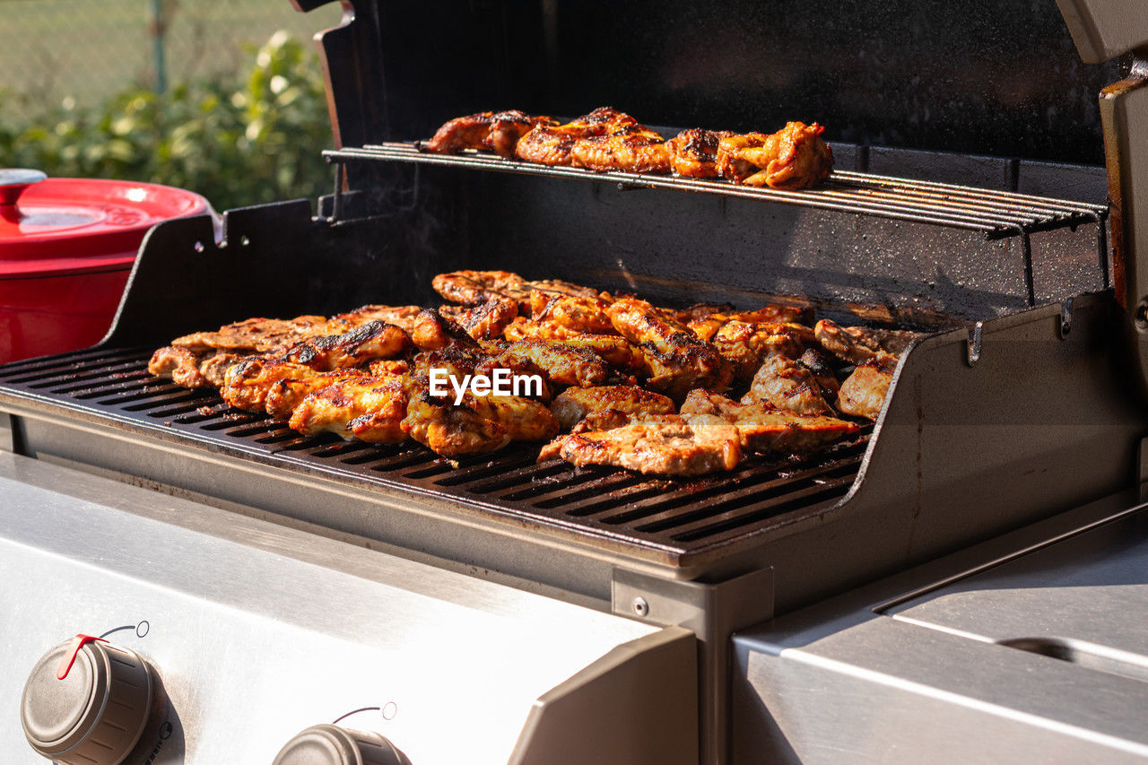 Perfectly seasoned chicken grilling on an outdoor gas barbecue under a sunny sky.
