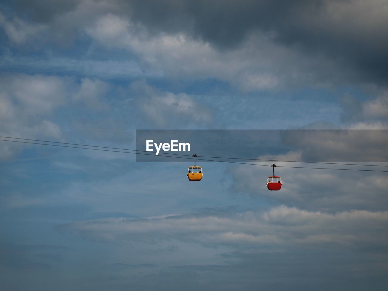 Low angle view of overhead cable cars against cloudy sky