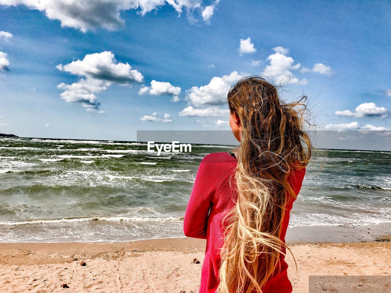 Rear view of woman with tousled hair standing at beach against sky