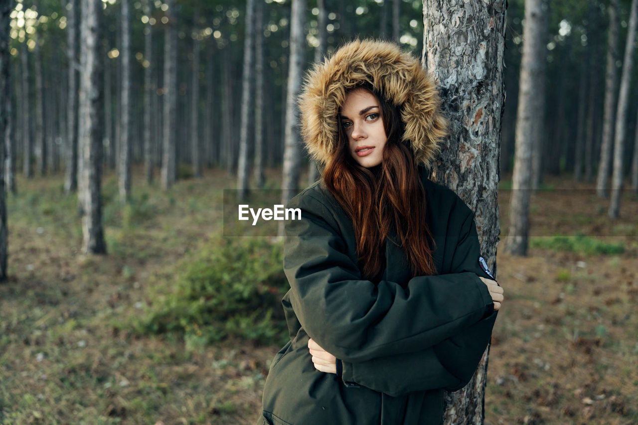 Young woman standing by tree trunk in forest