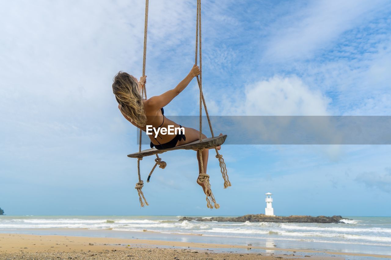 Low angle view of woman swinging at beach against sky