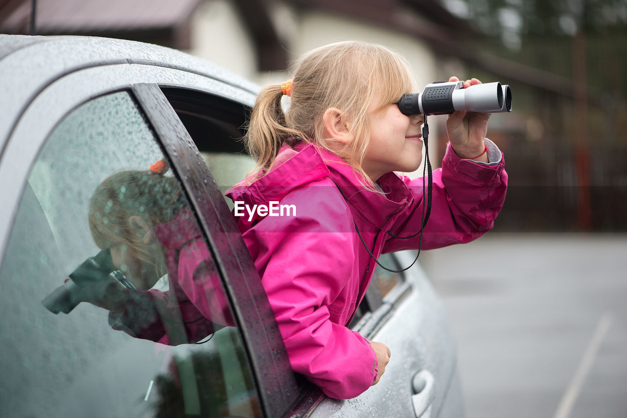 Sid view of girl looking through binoculars while traveling in car