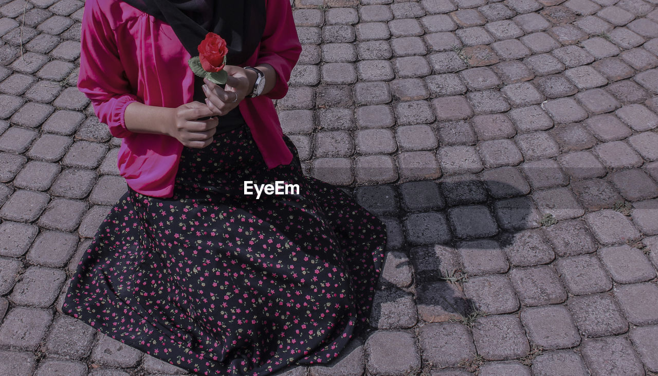 Midsection of woman holding rose while kneeling on footpath