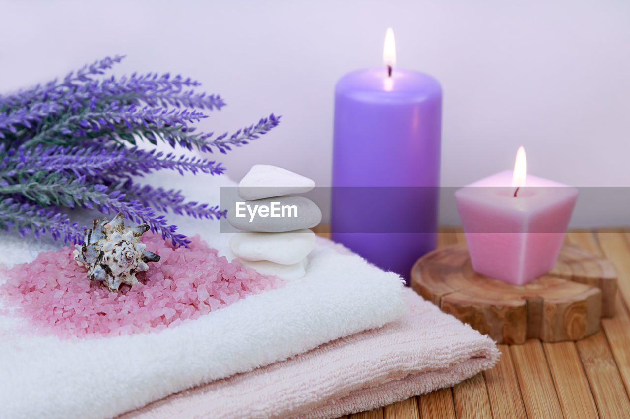 Candles with salts and flowers by towel on table