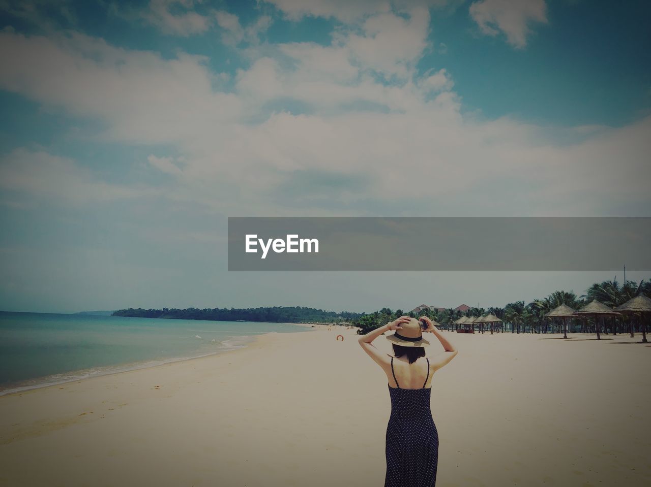 Rear view of woman standing at beach against sky