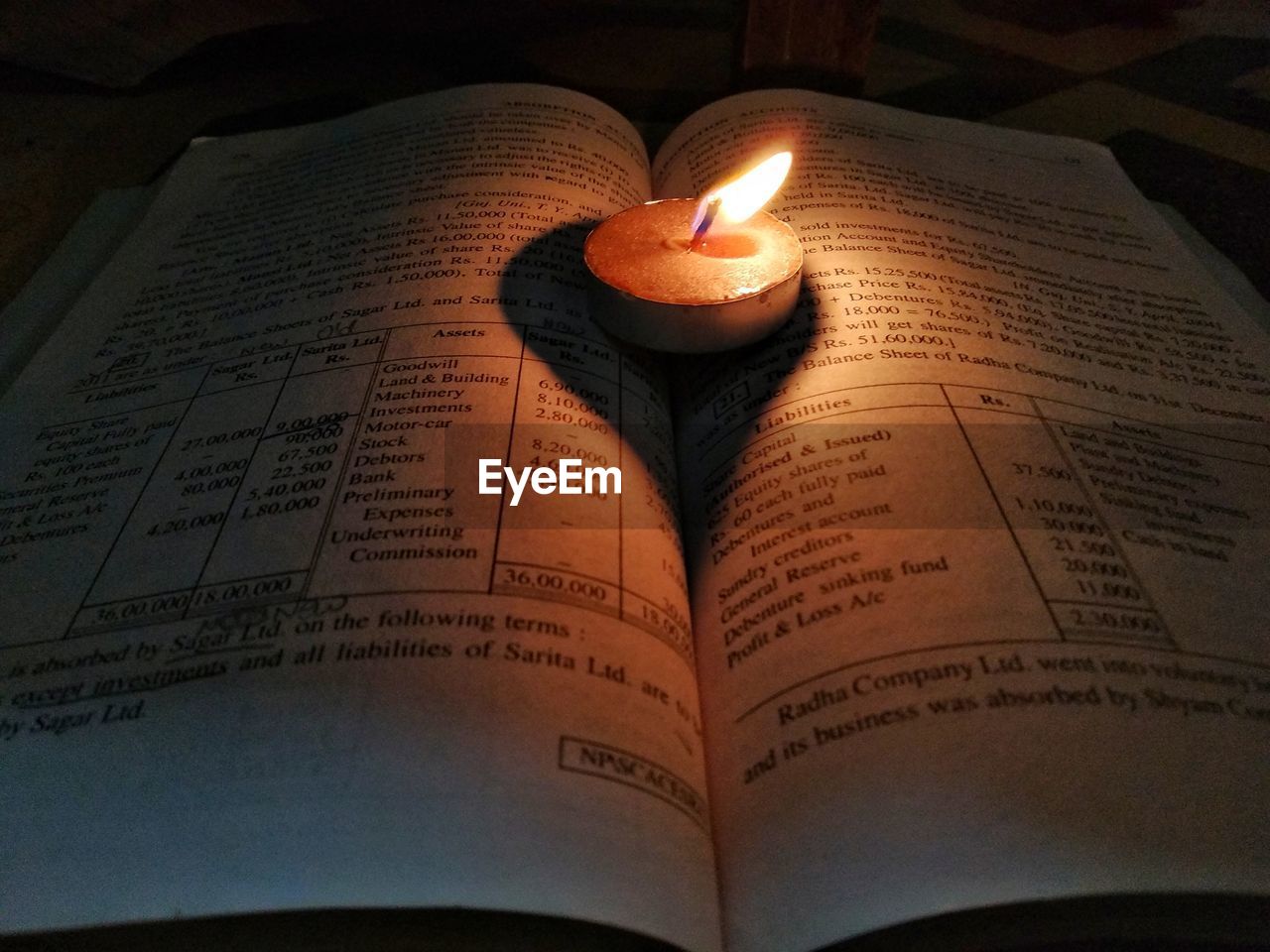 Close-up of lit tea light on open book in dark