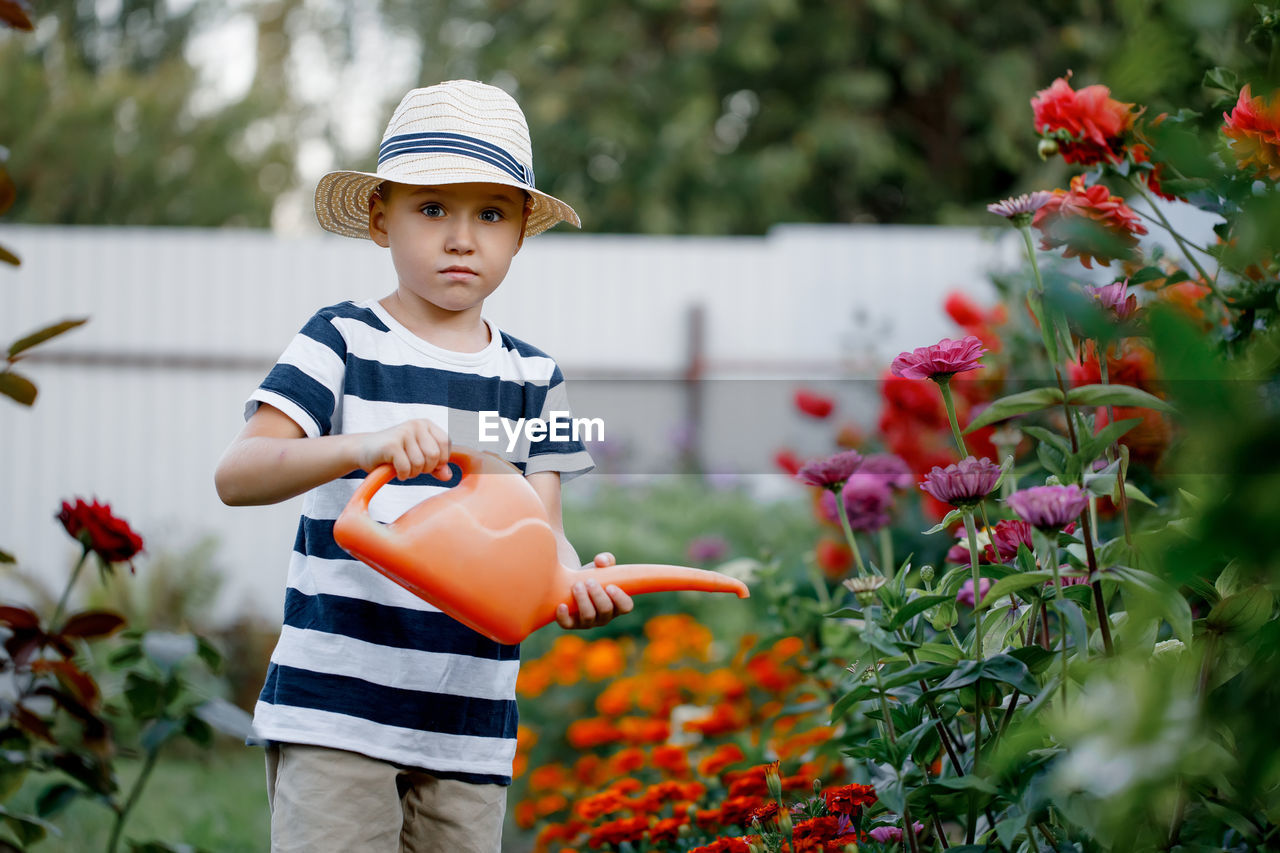 Cute little boy watering flowers with a watering can on a sunny summer day