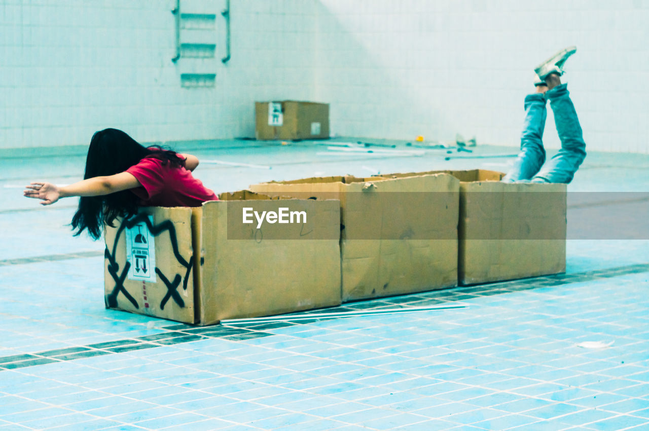 Playful friends playing with cardboard boxes on tiled floor