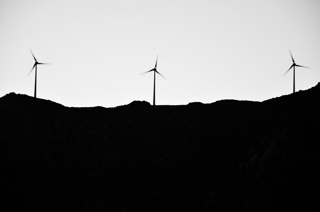 Silhouette wind turbines on landscape against clear sky