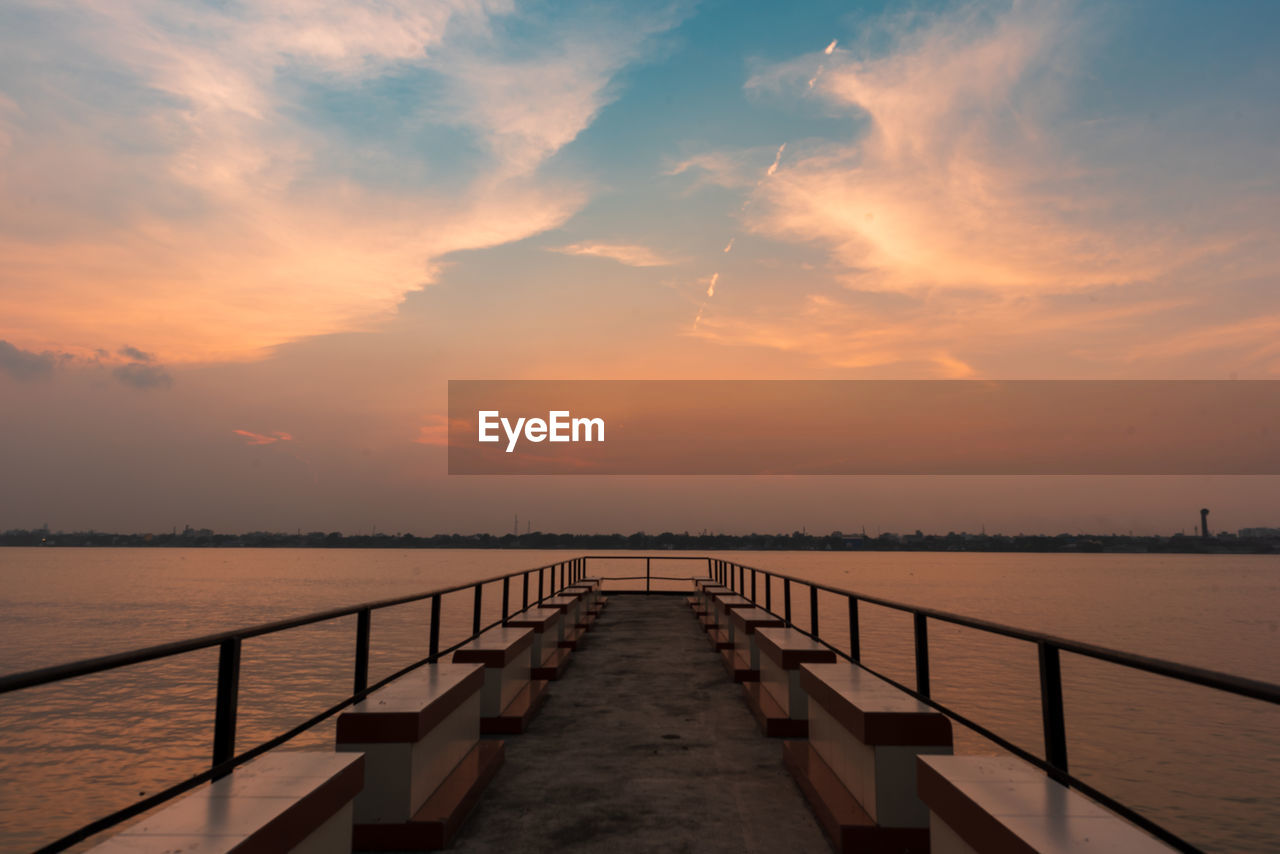 Pier over river against sky during sunset