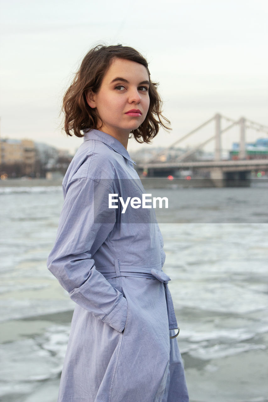 PORTRAIT OF YOUNG WOMAN STANDING AGAINST SEA